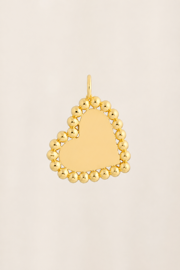 A gold heart-shaped pendant with a smooth, polished center and a border of small, rounded beads, shown on a light beige background.